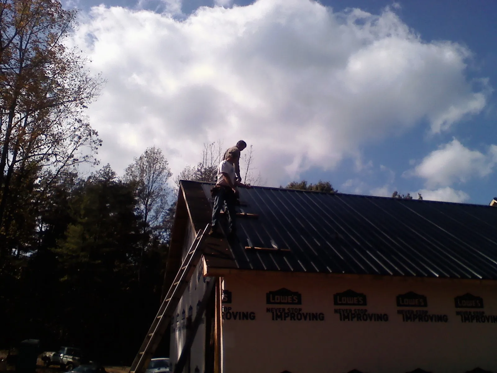 Roofer fastening dark metal panels high against a cloudy sky, from a Roof Inspection job in Adairsville