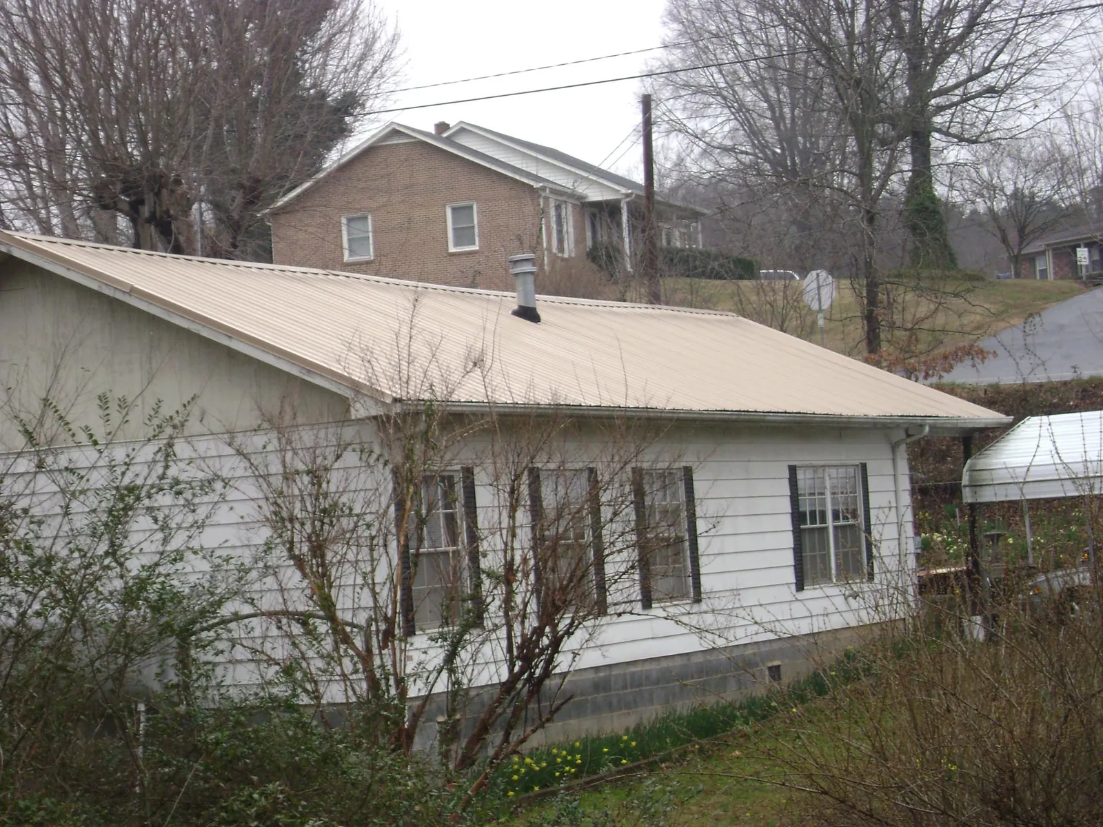 Tan metal roof on a white sided house set into a hillside — Commercial Roofing by Roofing Brothers in Adairsville